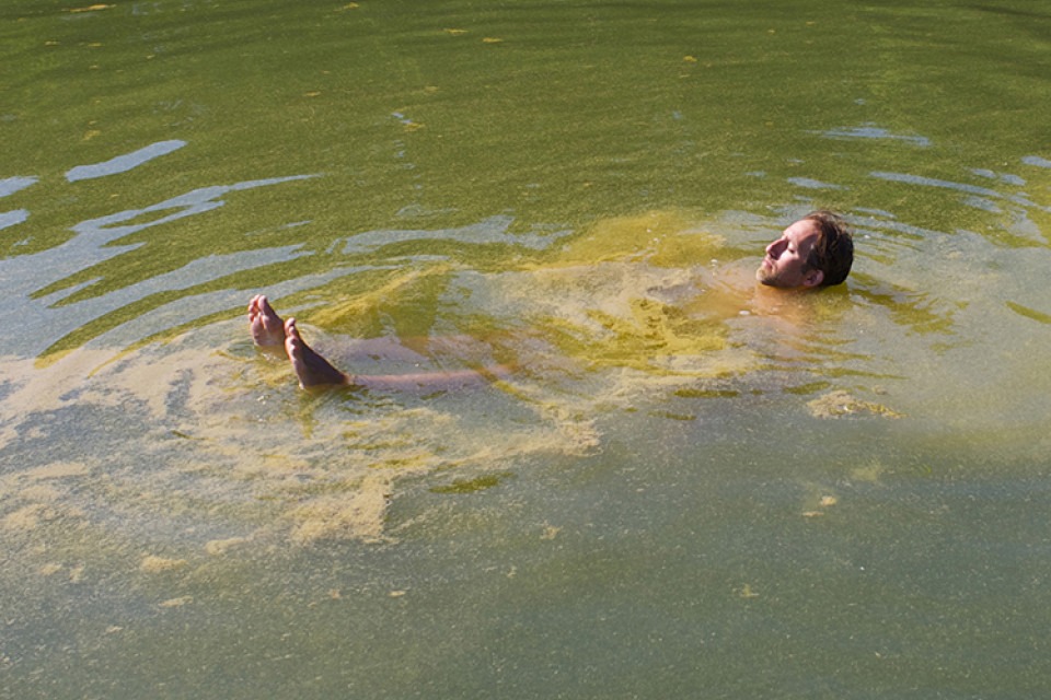 Man som ligger och flyter i vatten med kraftig algblomning